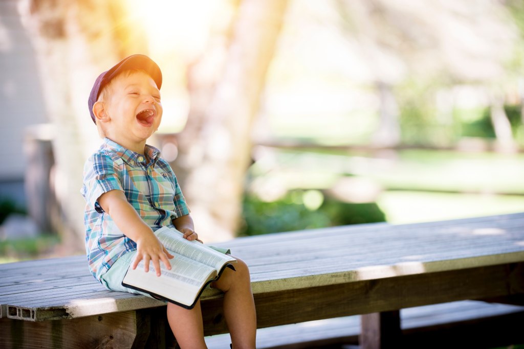 Boy sitting on bench laughing at a book